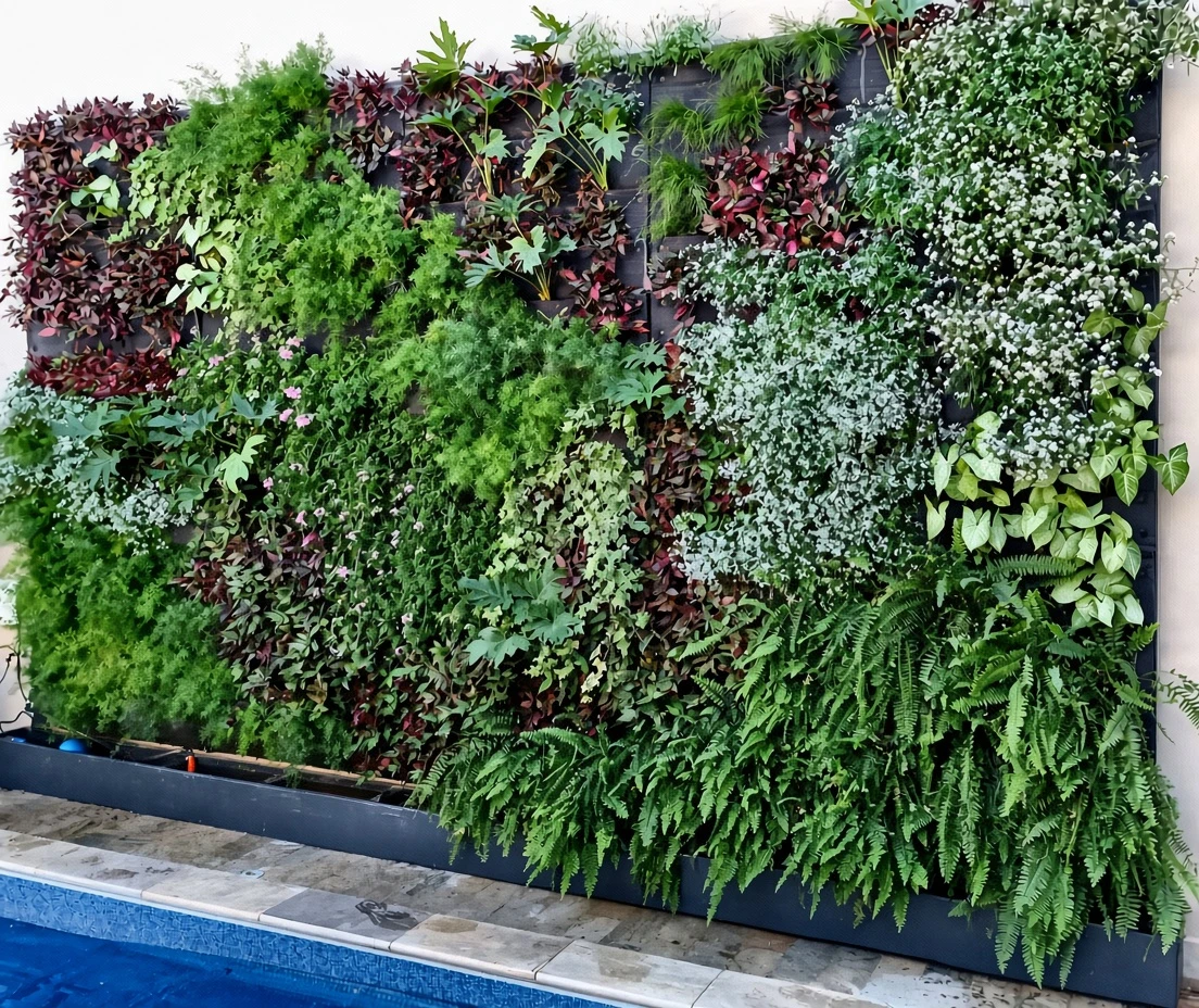 Jardim vertical com folhagens verdes, vinho e brancas sobre floreira junto à piscina